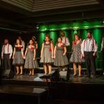 Chor Royal auf einer Bühne, die Frauen in Rockabilly Kleidern, die Herren in schwarzen Hosen und weißen Hemden mit roten Hosenträgern